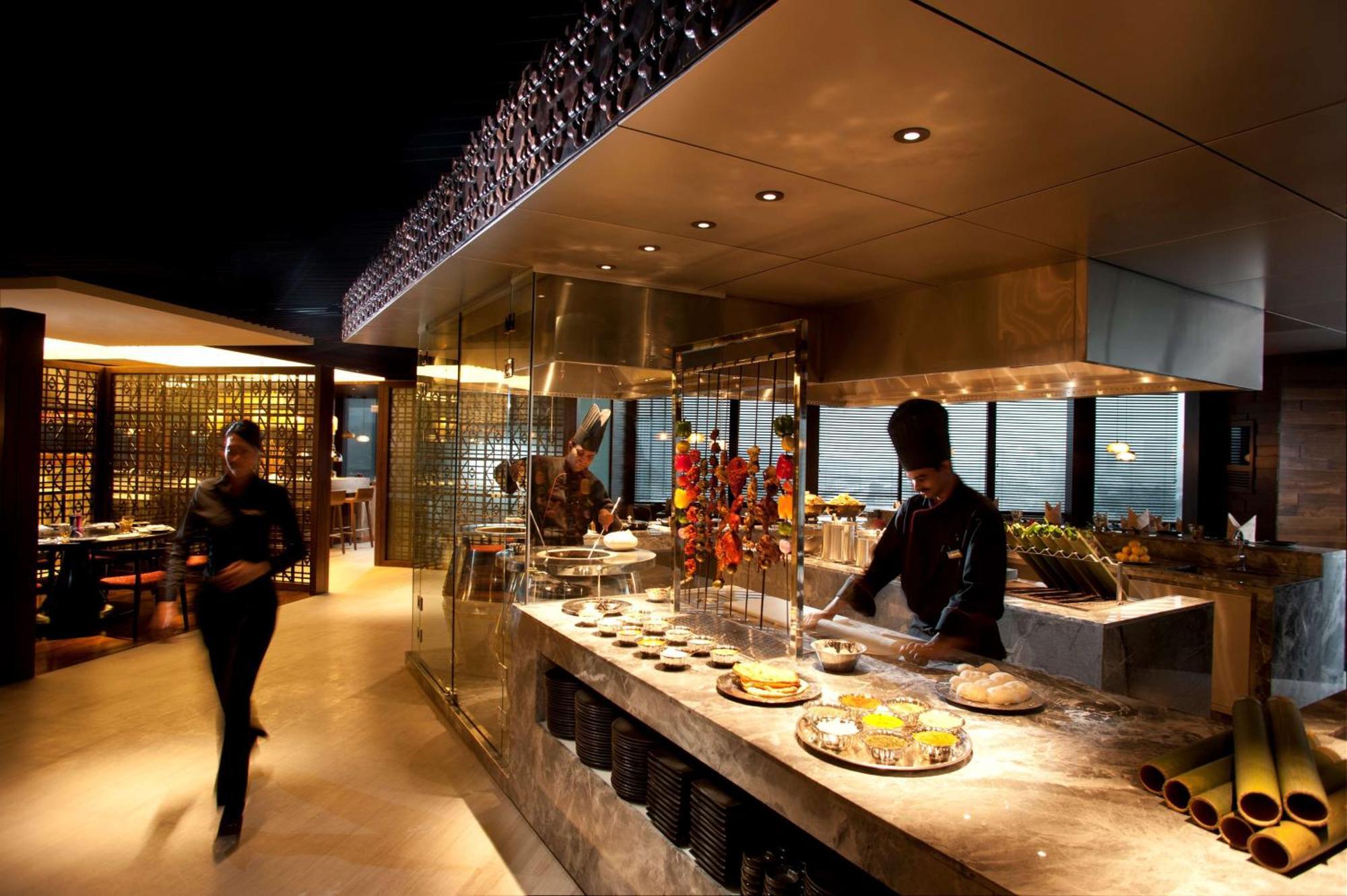 Doubletree By Hilton Kuala Lumpur Hotel Екстериор снимка The photo depicts a modern restaurant interior with a sleek and sophisticated design. In the foreground, there is a chef working at an open kitchen area, preparing food. The kitchen features a glass display that showcases a variety of dishes, along w