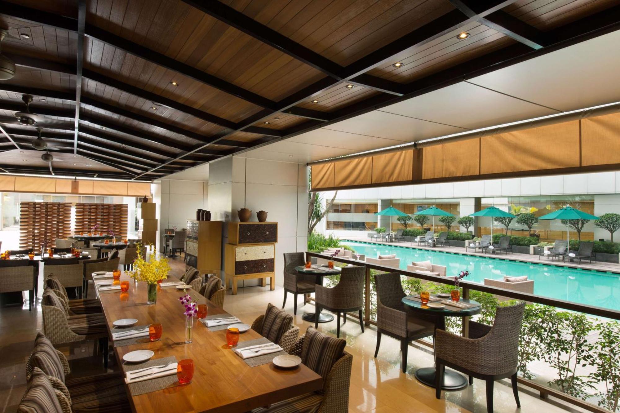Doubletree By Hilton Kuala Lumpur Hotel Екстериор снимка The photo shows an indoor restaurant area with a modern and stylish design. There are several tables set for dining, featuring place settings and drinks. Large windows allow for a view of a swimming pool outside, which is adorned with umbrellas. The 