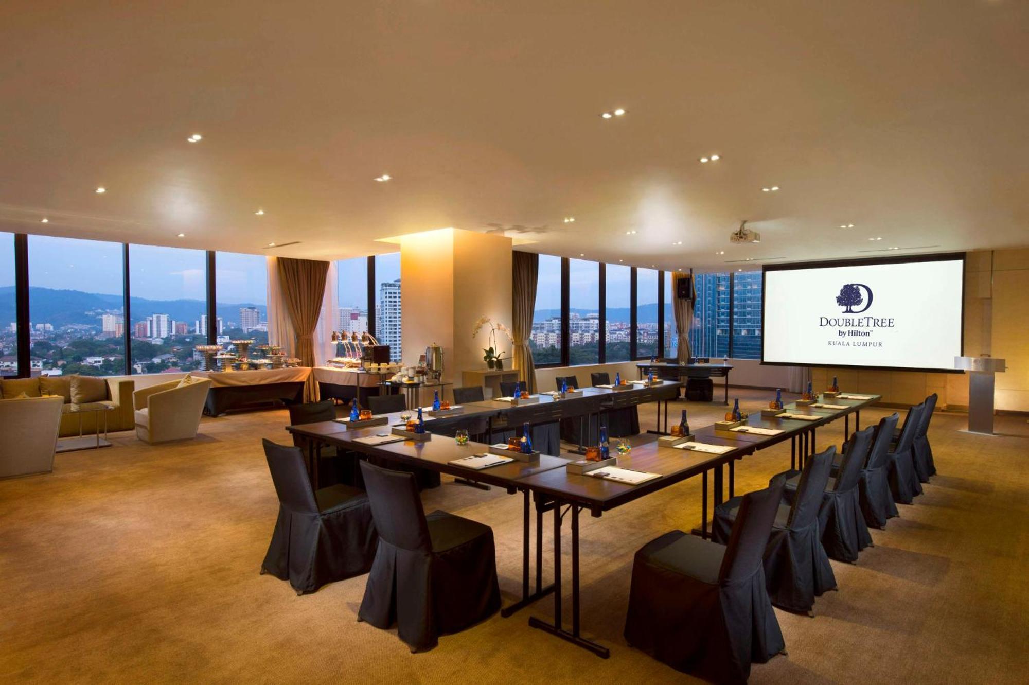 Doubletree By Hilton Kuala Lumpur Hotel Екстериор снимка The photo shows a modern conference room. It features a long table arranged for a meeting, with black chairs and notepads placed at each seat. The room has large windows that let in natural light and offer a view of the city outside. On one wall, the